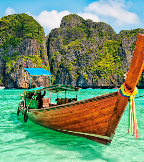 Traditional longtail boat on the Andaman Sea in Phuket during sunset, with vibrant orange and purple skies.