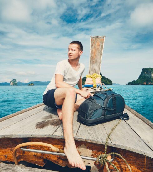 Young tourist experiencing his first time in Phuket, sitting on a traditional longtail boat surrounded by clear blue sea and limestone islands