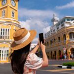 Tourist taking photo of the iconic yellow clock tower in Phuket Old Town, Thailand.