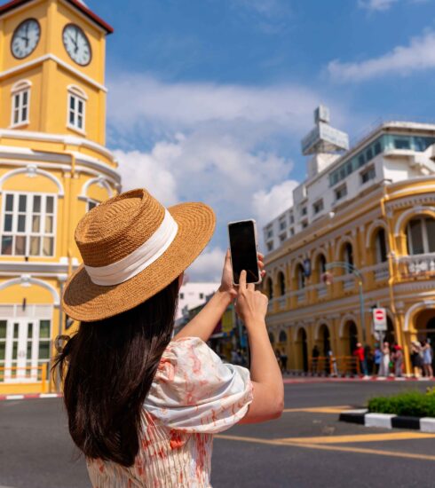 Tourist taking photo of the iconic yellow clock tower in Phuket Old Town, Thailand.